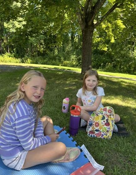 Two young girls sitting on a picnic blanket under a tree.