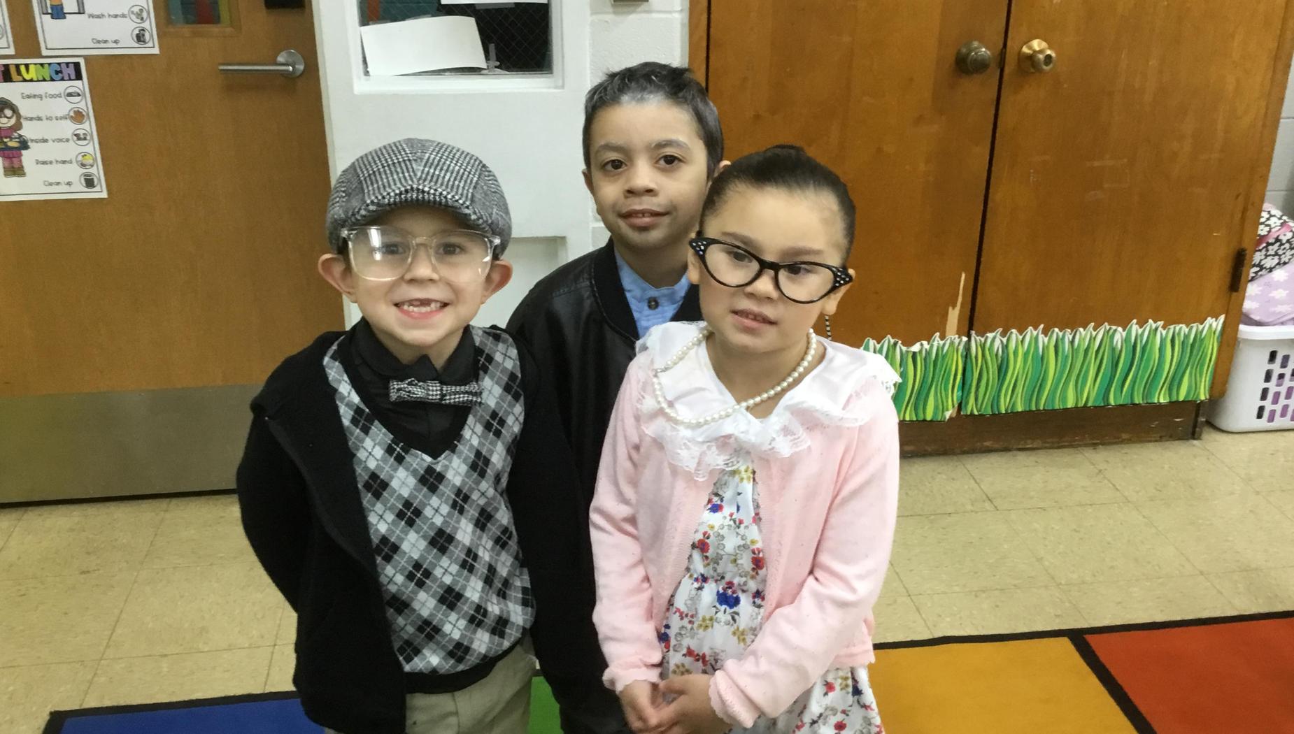 Three children dressed in vintage clothing smiling in a classroom setting.