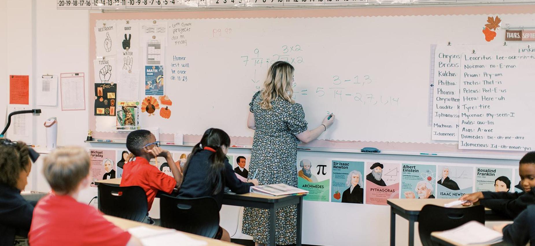 Teacher writing on the whiteboard as students follow along at their desks