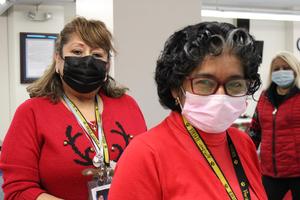 2 women wearing masks and red sweaters smiling at camera
