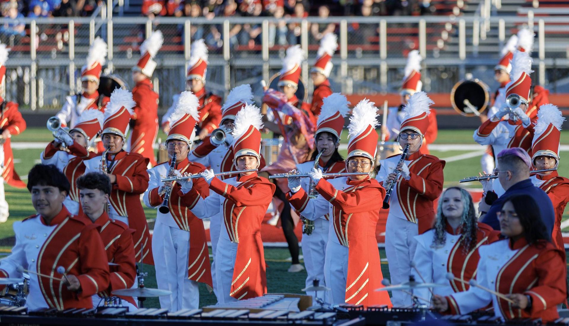 Marching band members in red uniforms perform on a field.