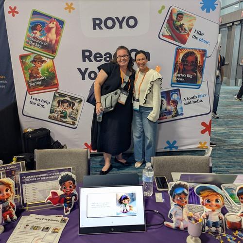 Mrs. Ratermann and a royo.ai representative in front of a backdrop advertising royo.ai