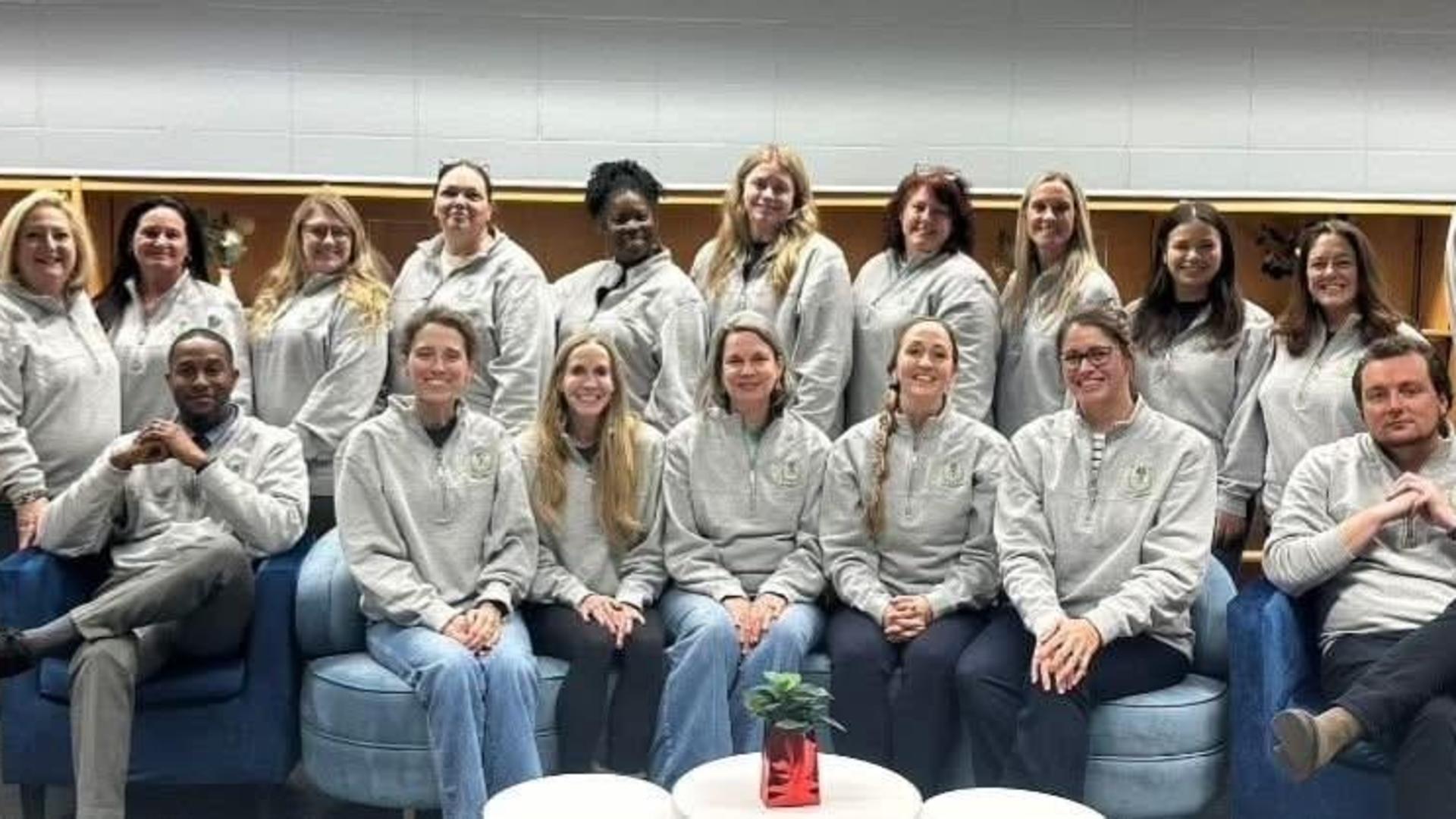Group of smiling individuals in matching gray sweatshirts seated and standing together.