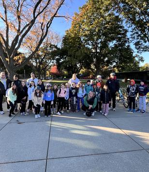 A large group of people in outdoor clothing and helmets poses in a park setting.