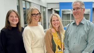 Four adults in professional dress smile at the camera