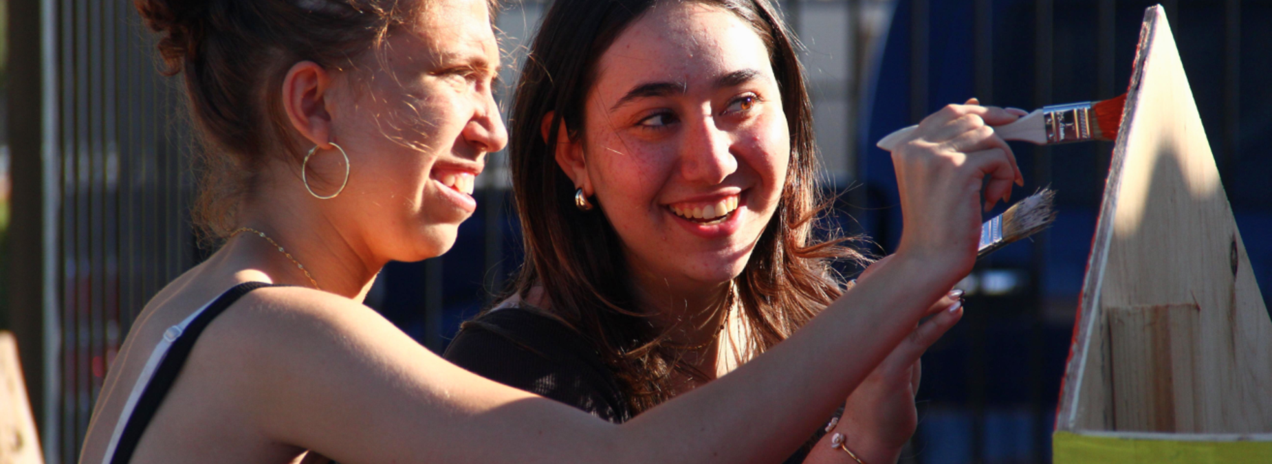 Two young women joyfully painting together outdoors.