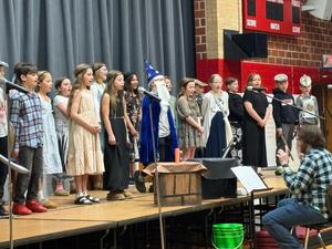 Performance scene with children singing in costumes on stage.