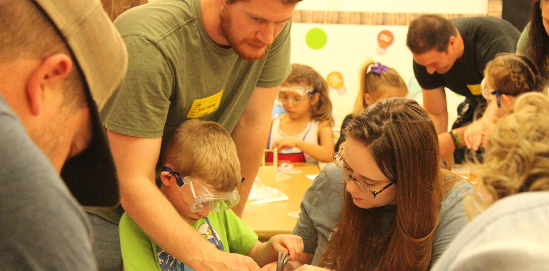 Adults and a child engaged in hands-on activities at a busy craft or learning station.