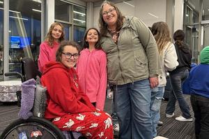 An adult and two children smile next to a high school student in a wheelchair.