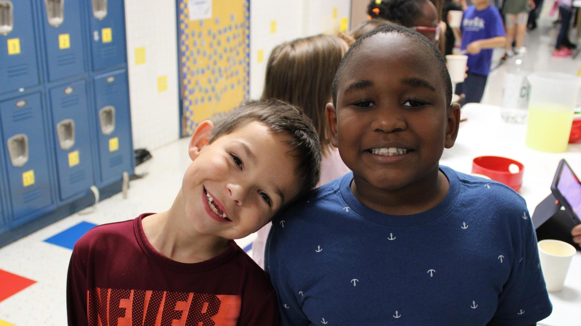 Two smiling boys posing together in a school hallway.