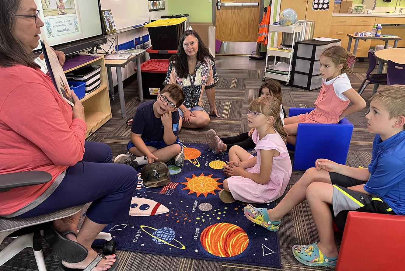 The teacher reads to students sitting on the floor around her.
