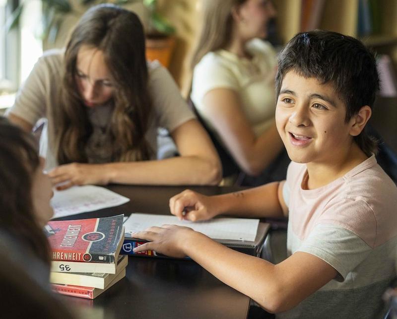 Two student sitting and working at a desk, one is smiling