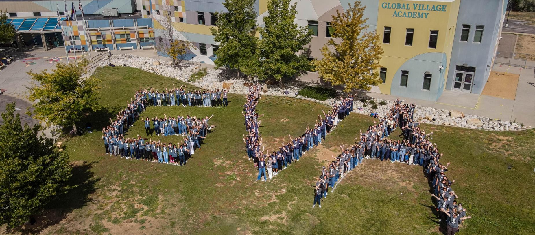 Students arranged to form the letters EVA outside a colorful school building.
