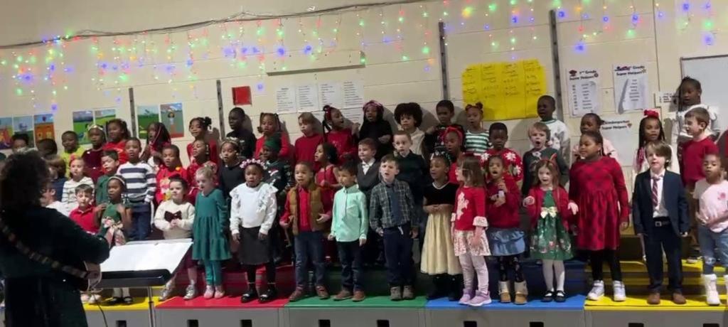 teacher plays the guitar in front of large group of singing children