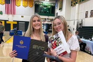 two girls stand in a gym and hold college admissions information