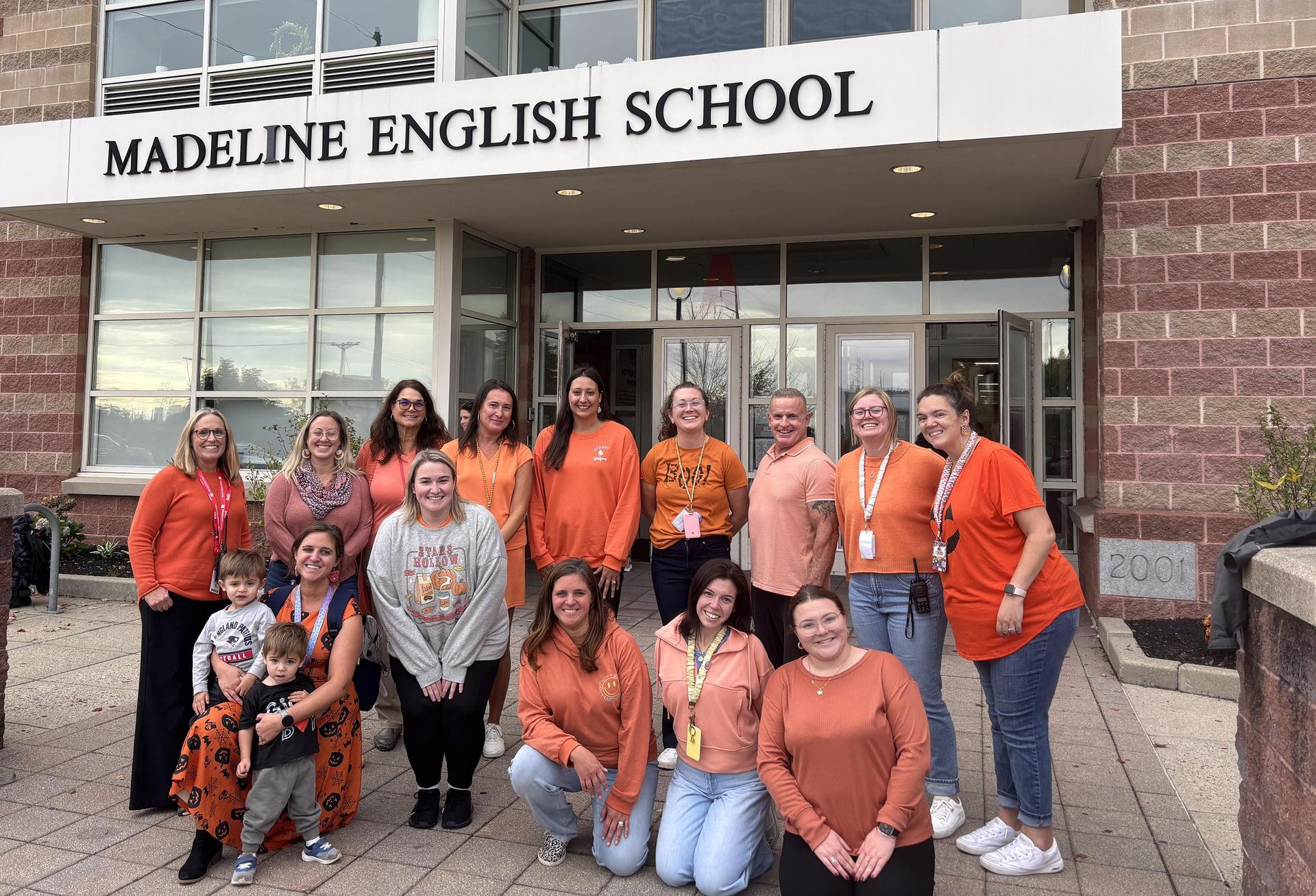 Large group of women in orange shirts outside the Madeline English School.