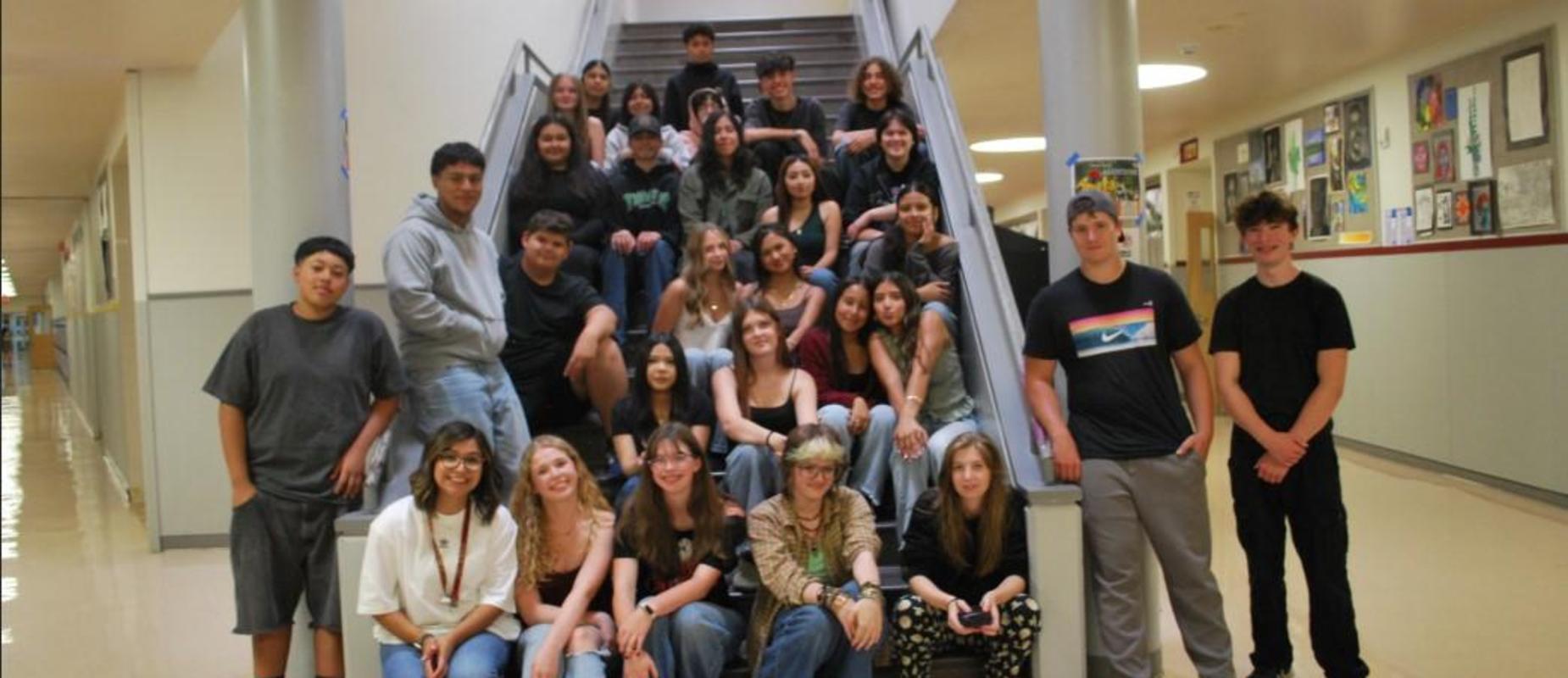 A diverse group of students sitting and standing on a staircase in a school hallway.