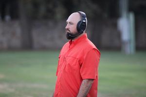 Man in an orange shirt wearing headphones stands on a field.