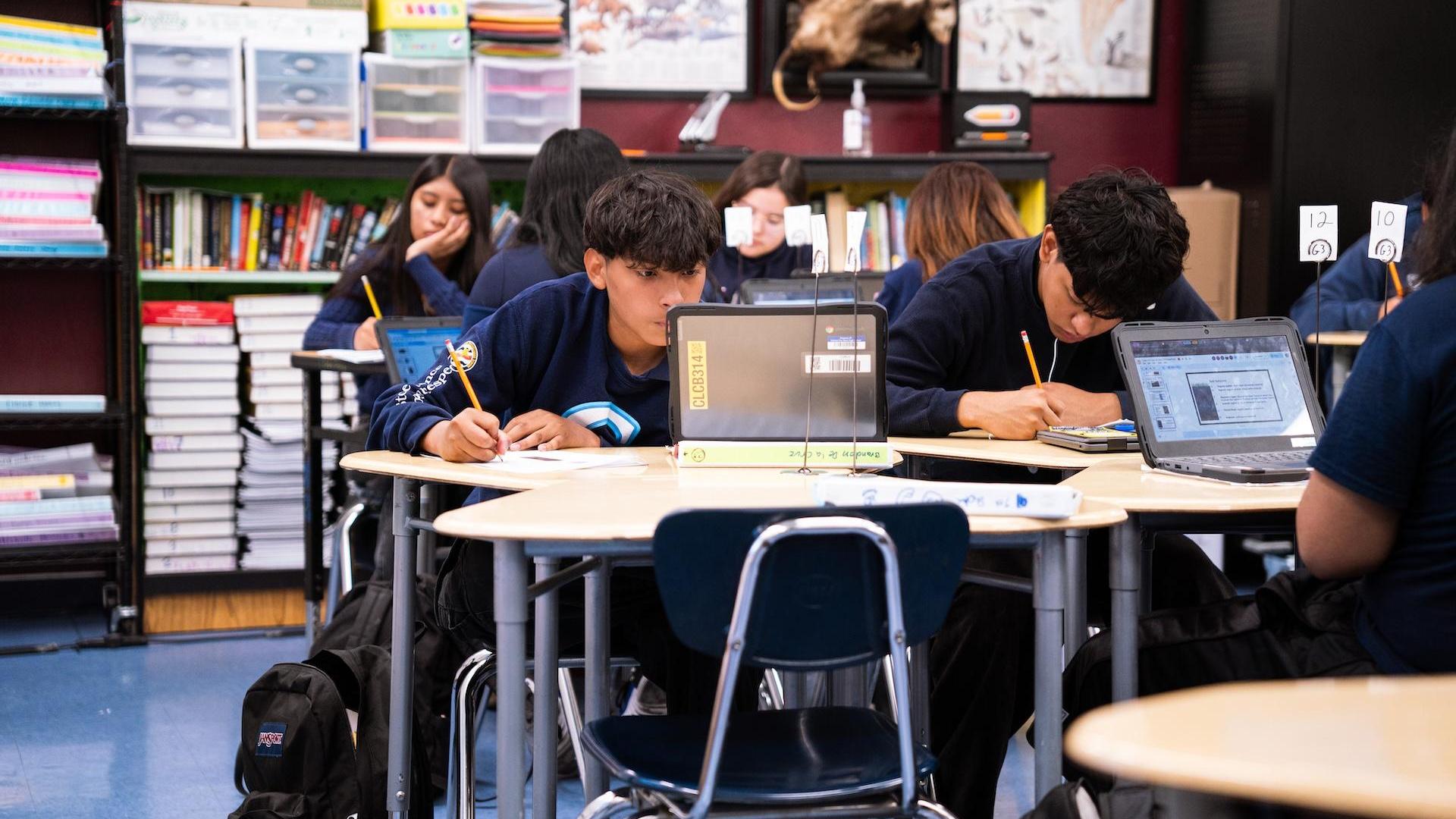 Students focus on assignments at desks in a classroom with various educational resources.