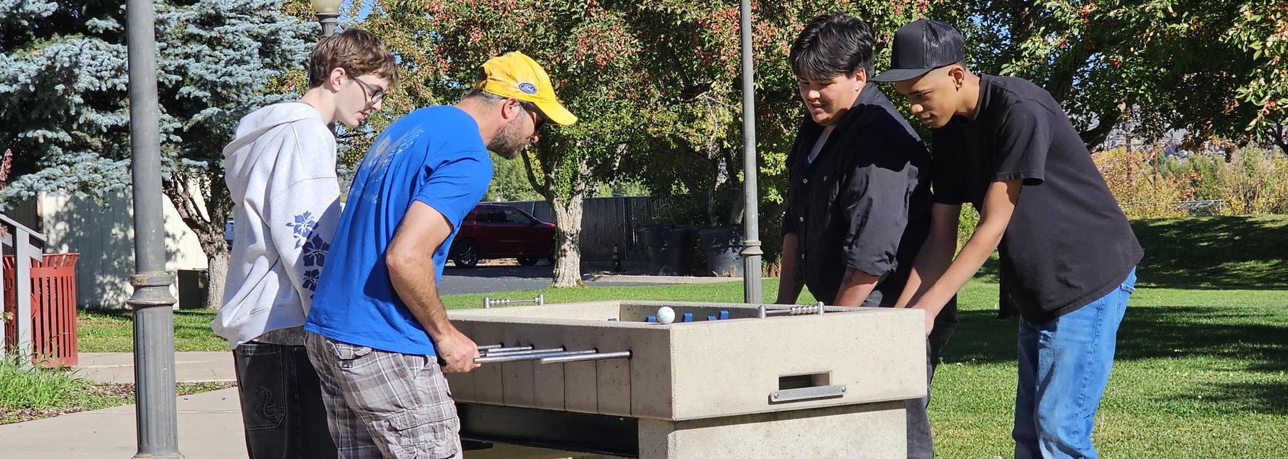 Taking a break to play foosball at a park table on a sunny day.