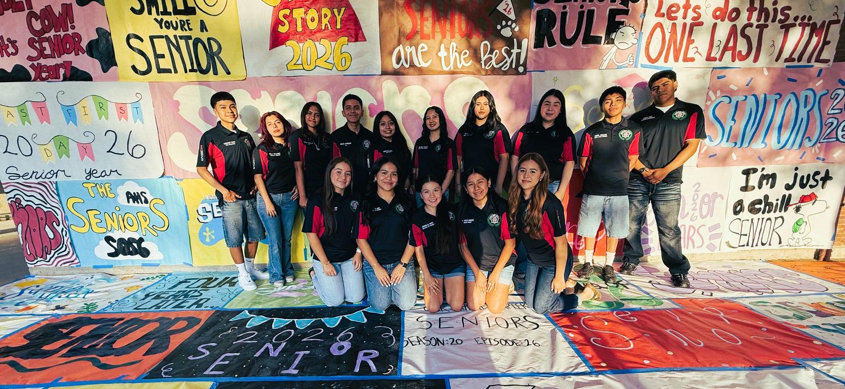 A group of high school seniors posing in front of a colorful mural celebrating their class.