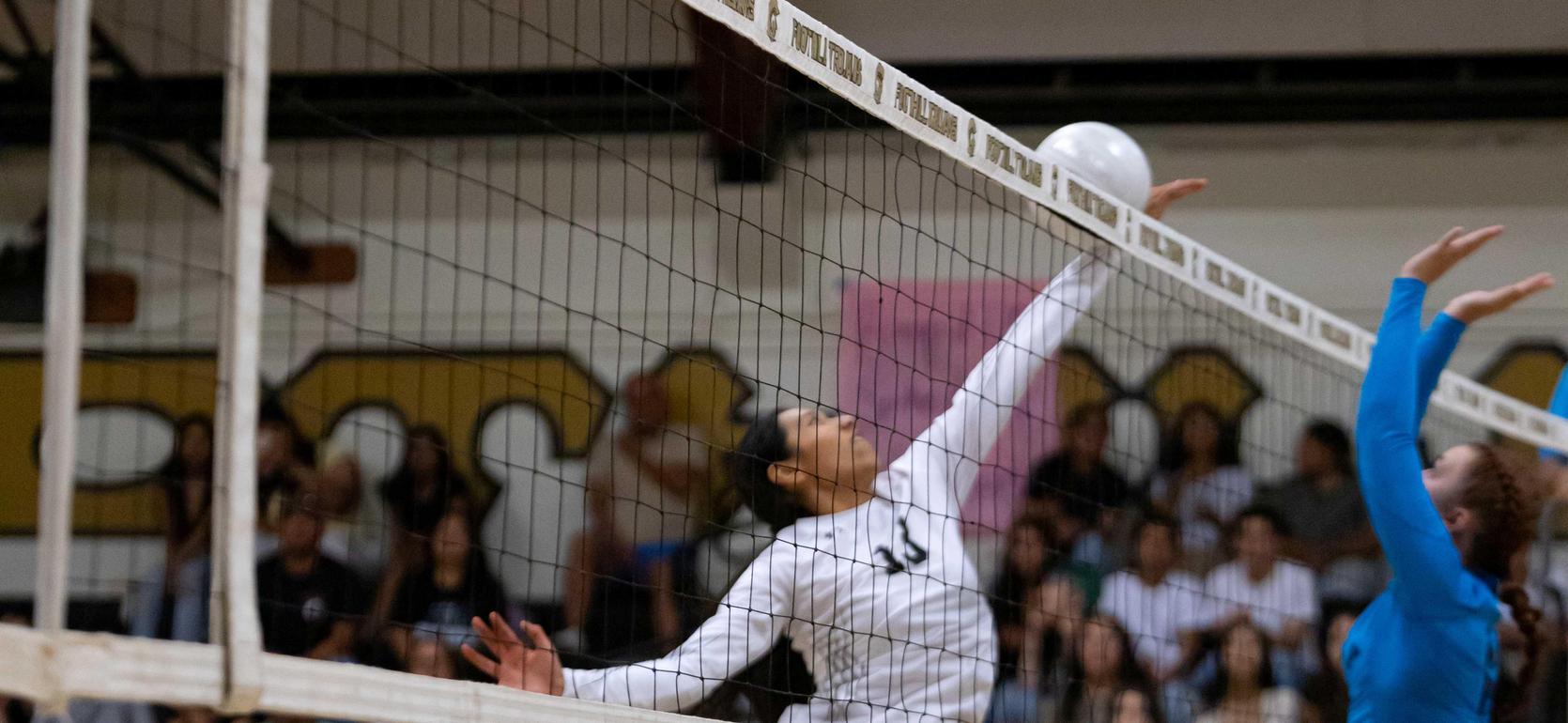 A volleyball player jumping to hit the ball at the net during a game.