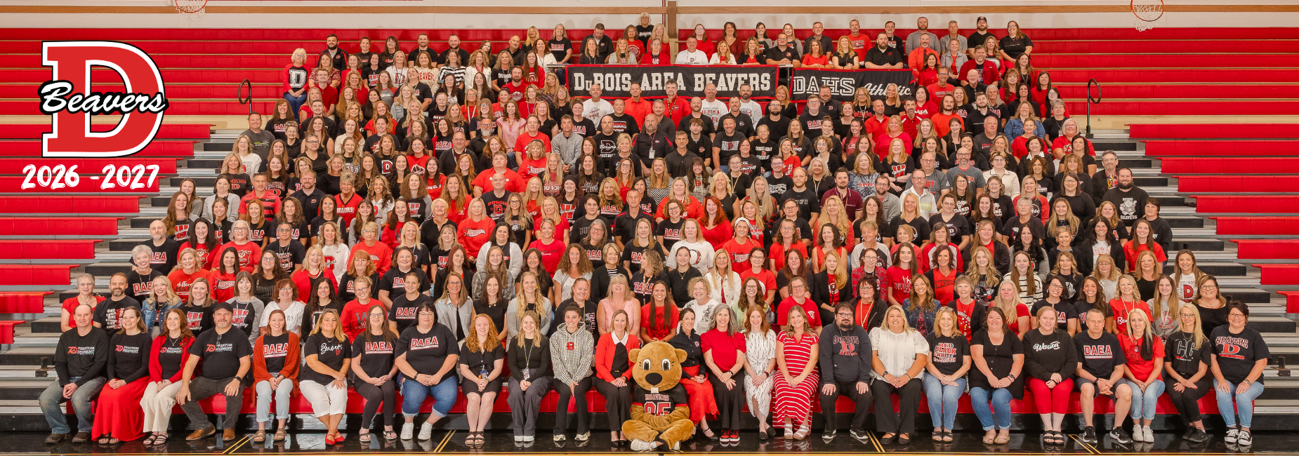 Large assembly 2026 2027 DASD Teachers and staff in red attire on bleachers.