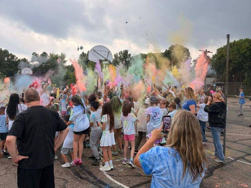 Crowd of children throwing colorful powder in the air during a celebration.