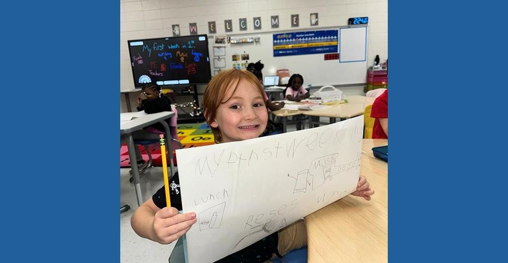 Child holding up their work and grinning with pride