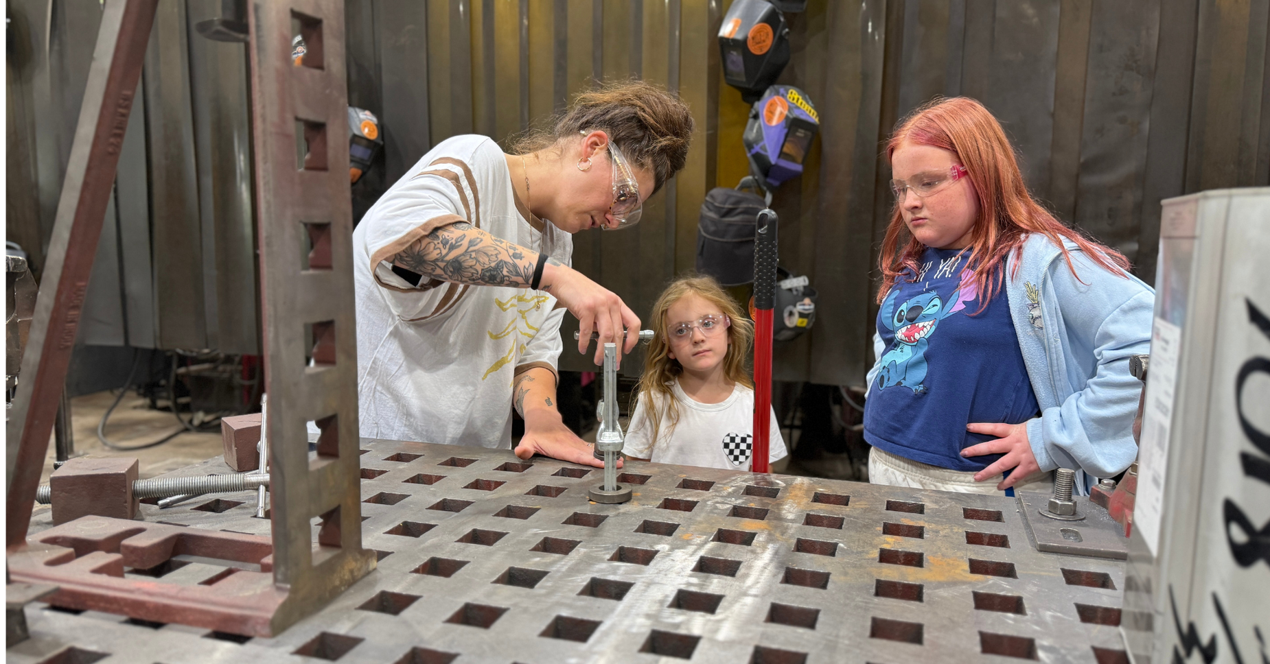 An adult and two children observing a hands-on activity in a workshop.