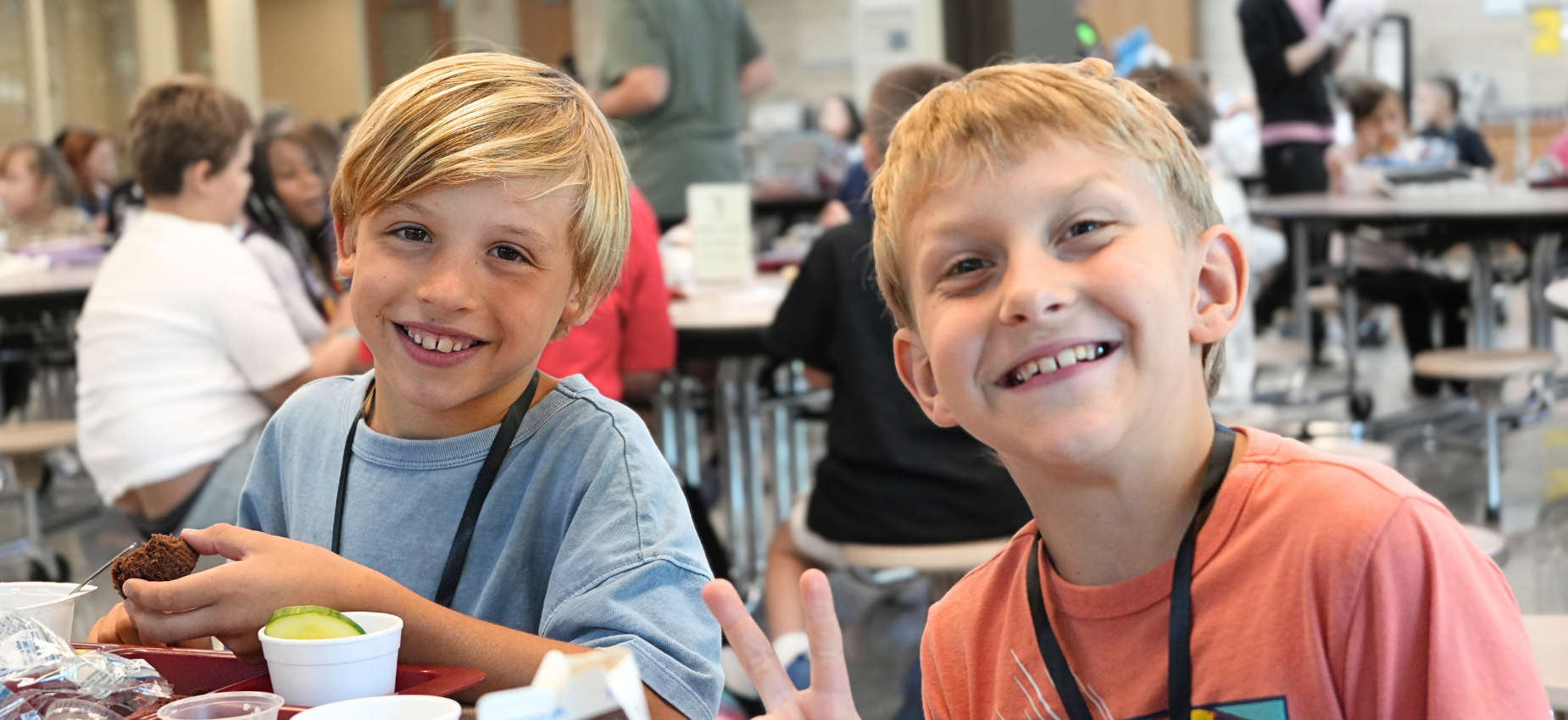 Two boys happily eat lunch at a school cafeteria.