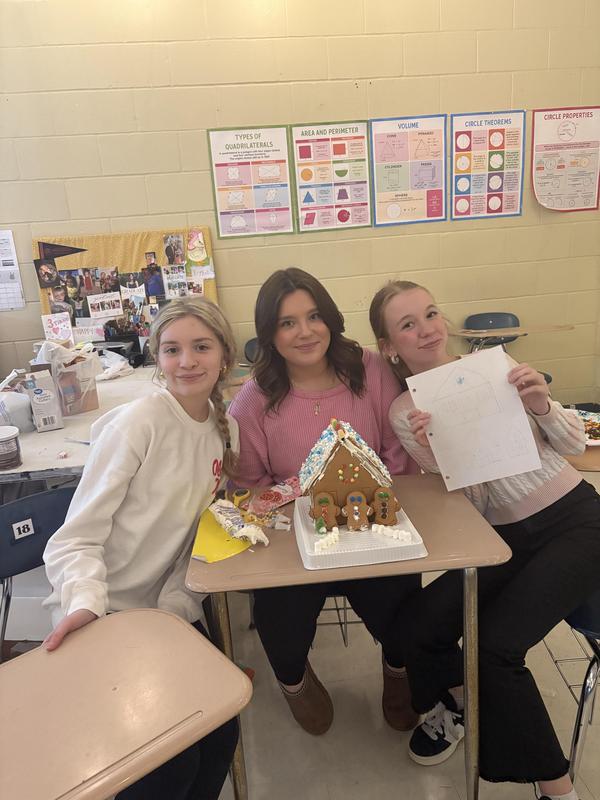 three students sitting in desks with gingerbread house and plans