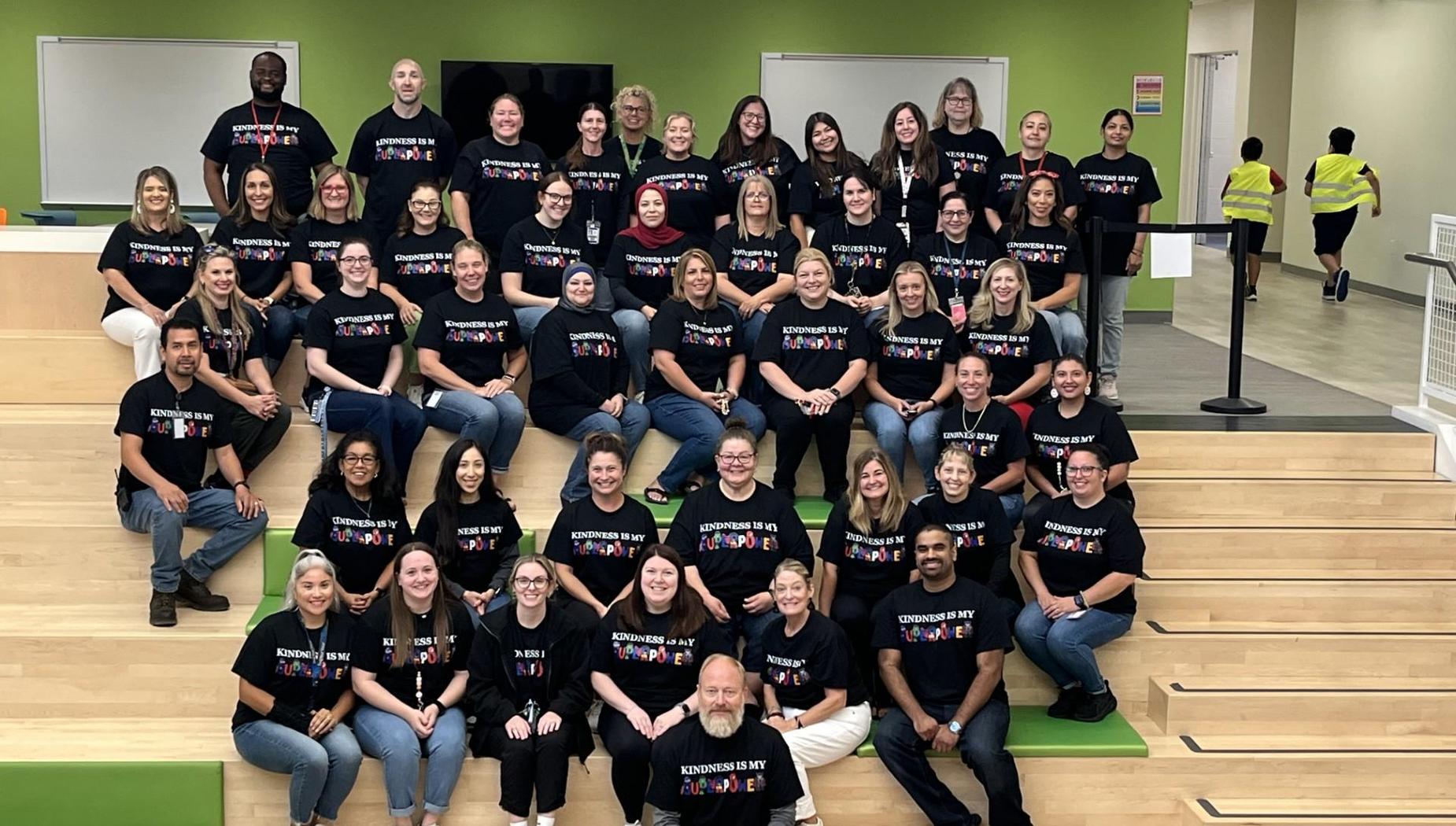 A large group photo of diverse individuals in matching black shirts, posing together.