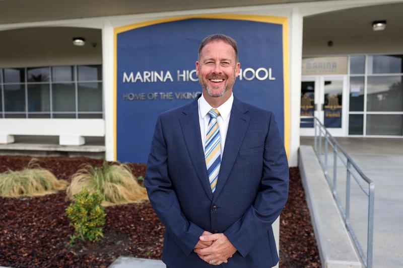 Rob Rasmussen smiles in front of Marina High School admin building