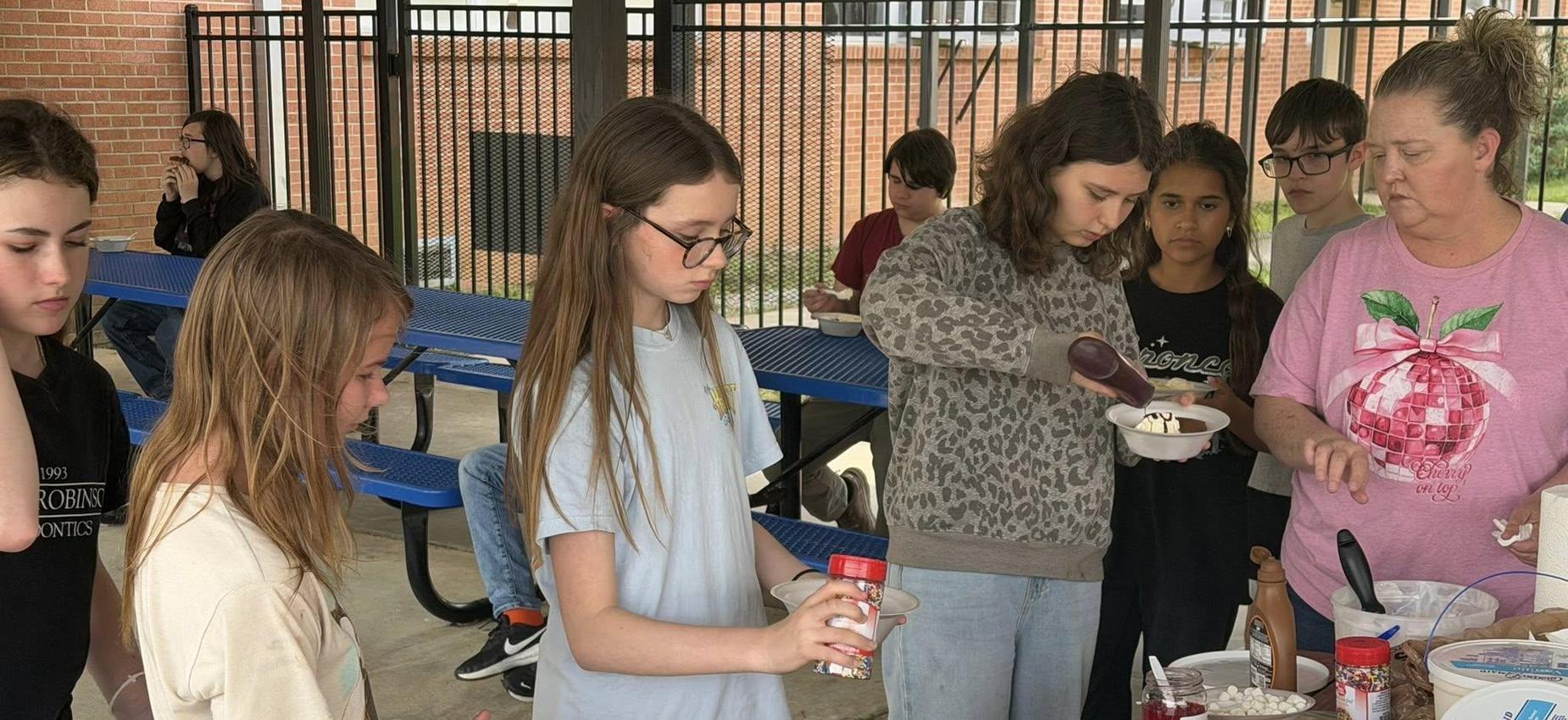 A group of children and adults preparing food at a table outdoors.