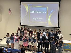 Image of 24 students inducted into NHS standing in front of a screen with text that says NHS Induction May 13, 2026