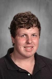 Smiling man with curly hair wearing a black polo shirt.