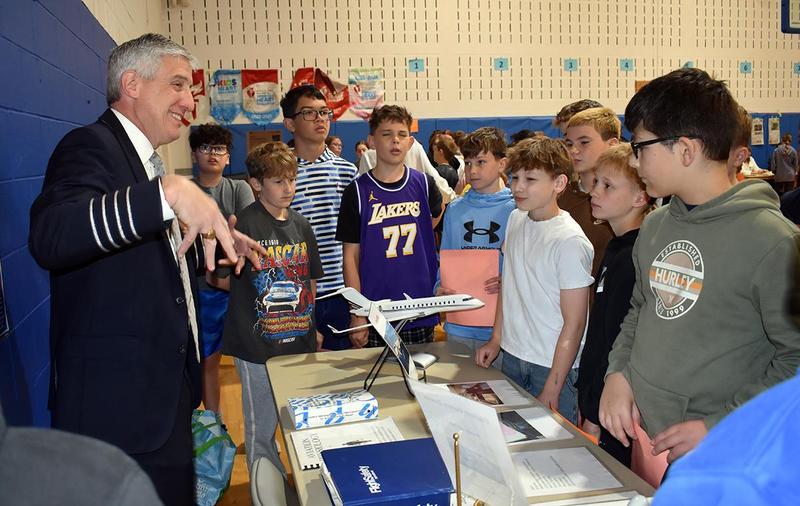 A group of students listening intently to a pilot explaining an aircraft model.
