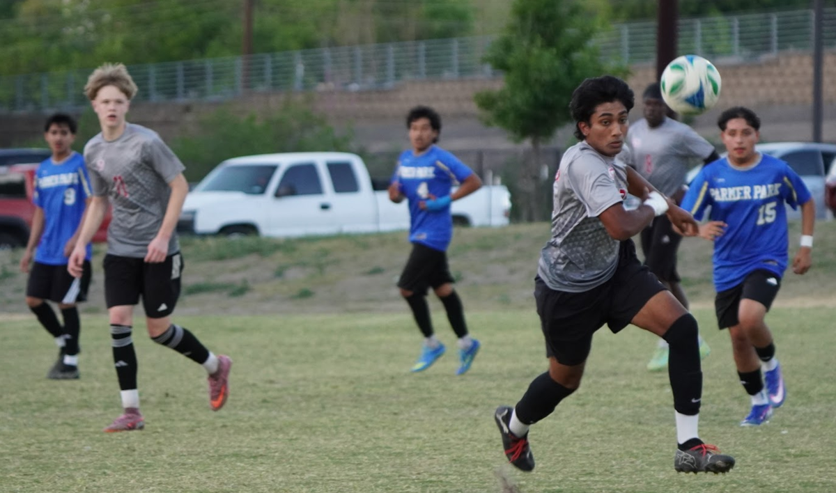BOys run on a soccer field with a ball at eye-level on the right side