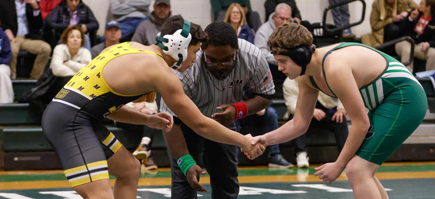 Two young wrestlers in a match preparing to grapple, with a referee overseeing.