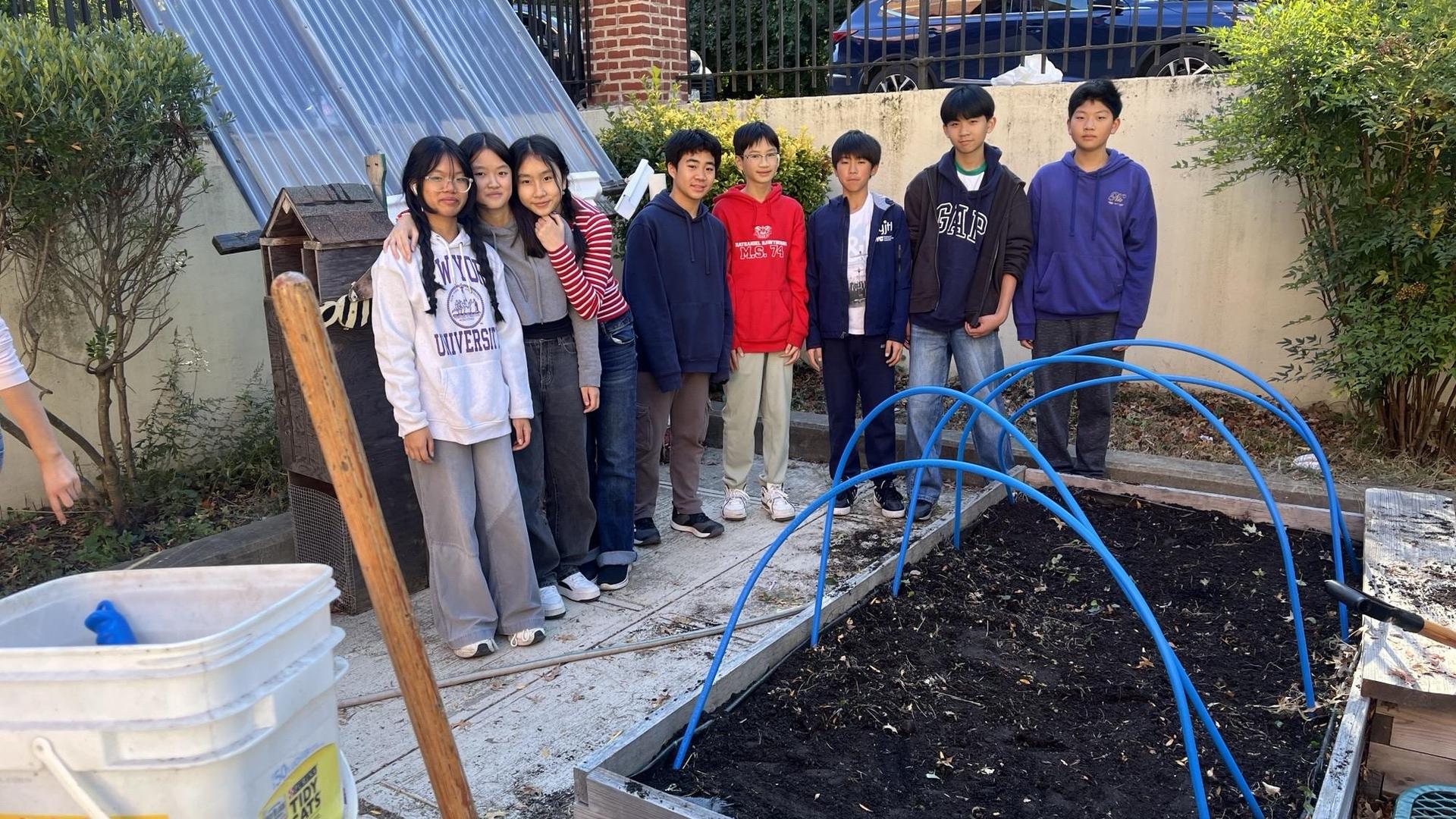 Students stand together in a garden near planting beds with blue hoops.