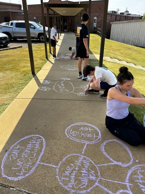 Multiple students writing on concrete with chalk