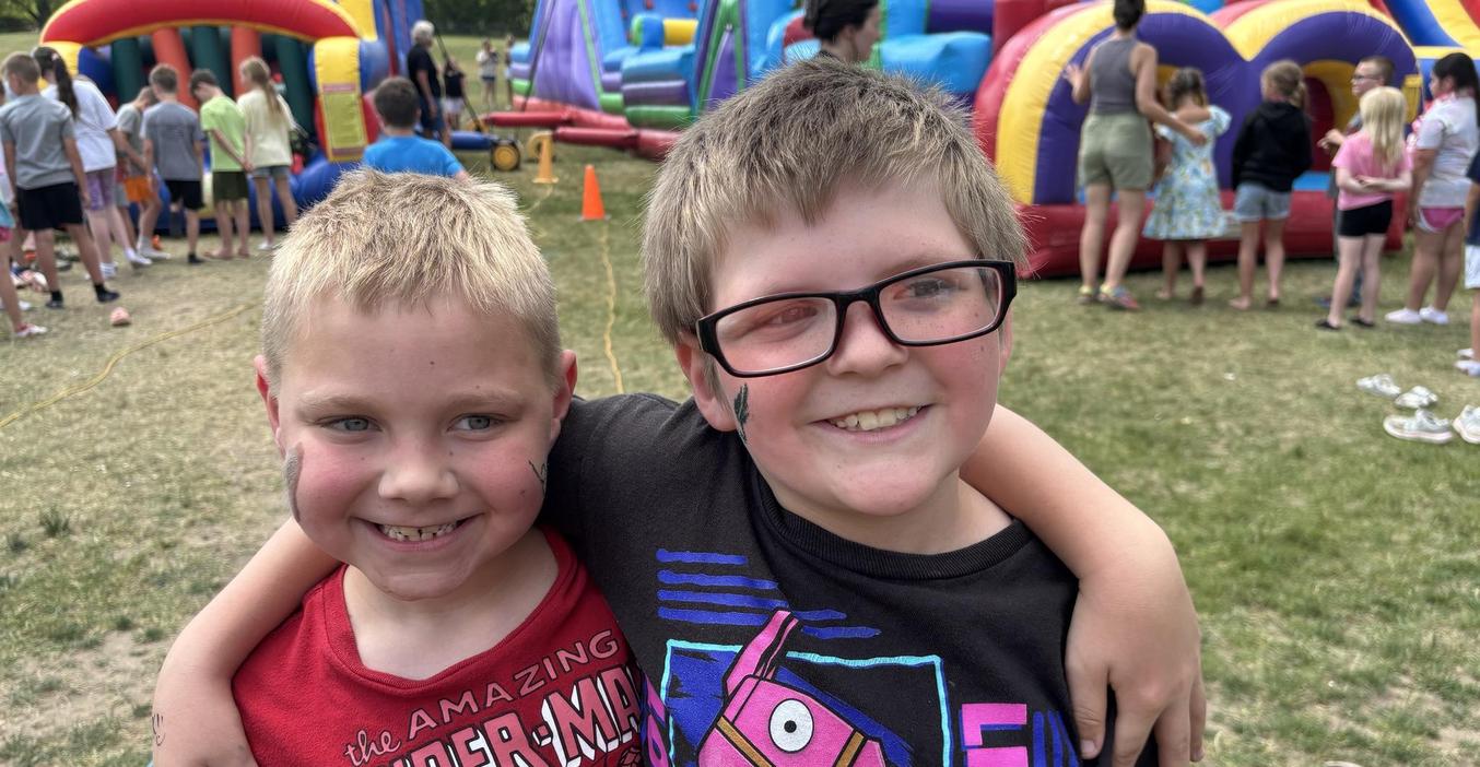 Two happy boys with arms around each other, smiling at a fun fair setting.