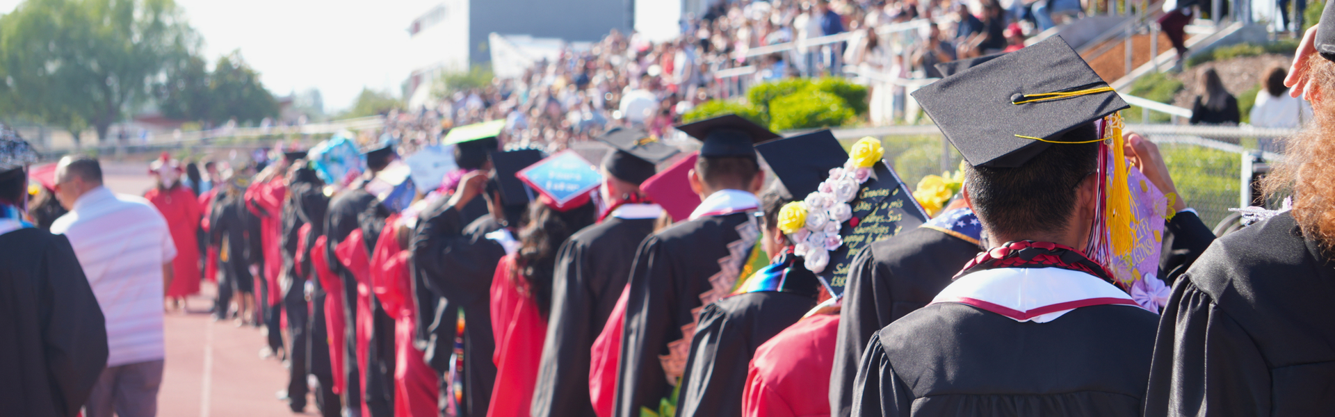 Line of graduates in caps and gowns walking across a field.