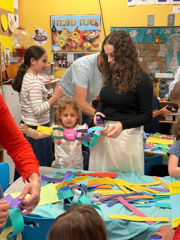 A kindergartener works together with her older sister to make a chain out of felt strips for her Sukkah
