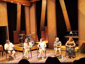 Four people seated on stage, with musical instruments in the background.