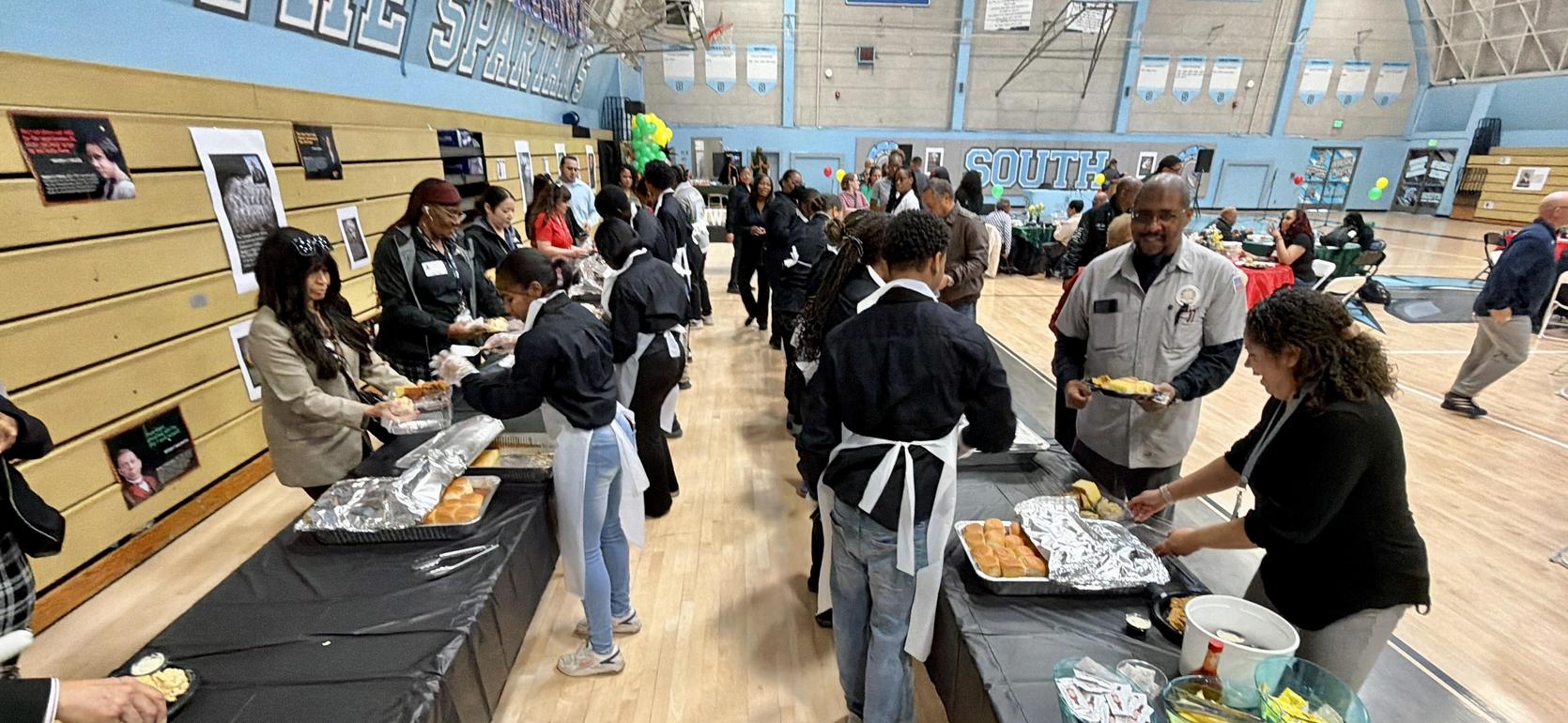 A community event with people serving food at tables in a gymnasium.