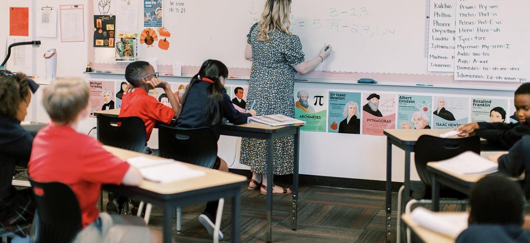 Teacher writing on the whiteboard as students follow along at their desks