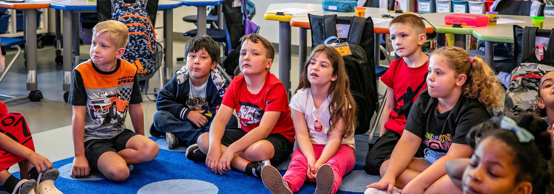 Group of children sitting on a carpet, engaged in an activity during class.