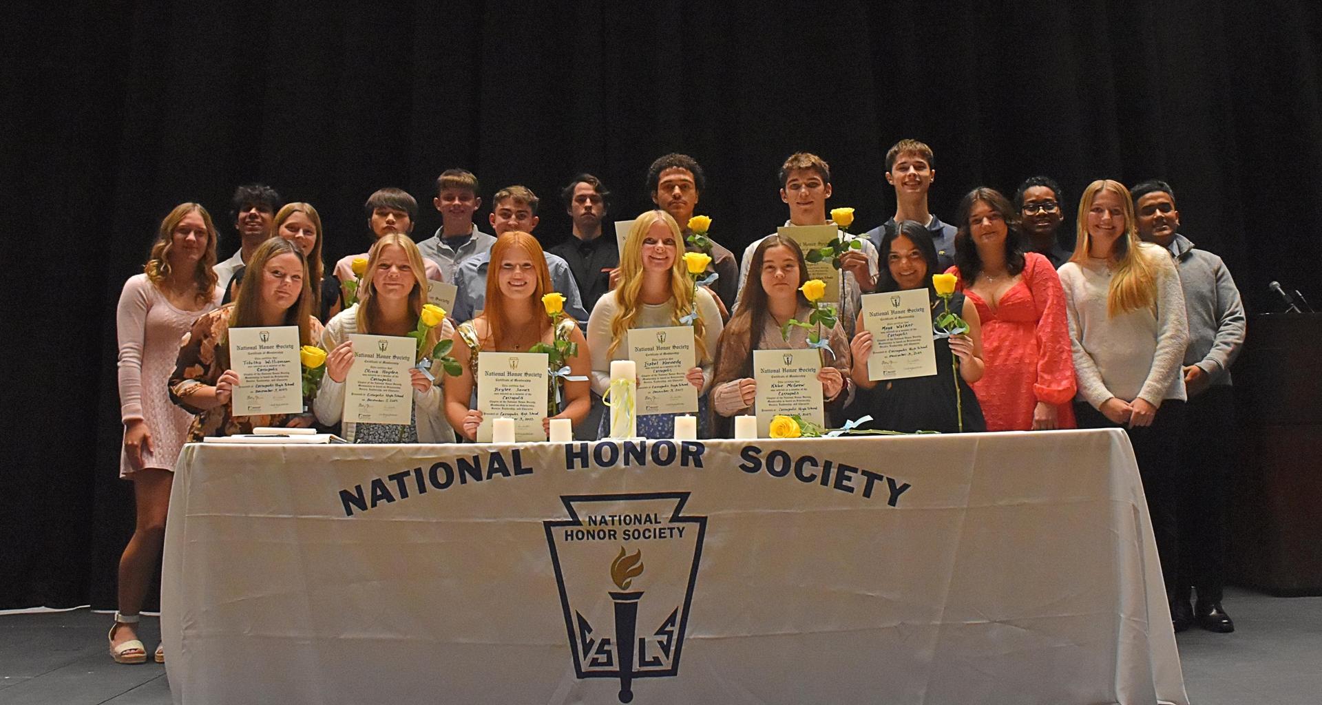 Students holding certificates and yellow roses at a National Honor Society ceremony.
